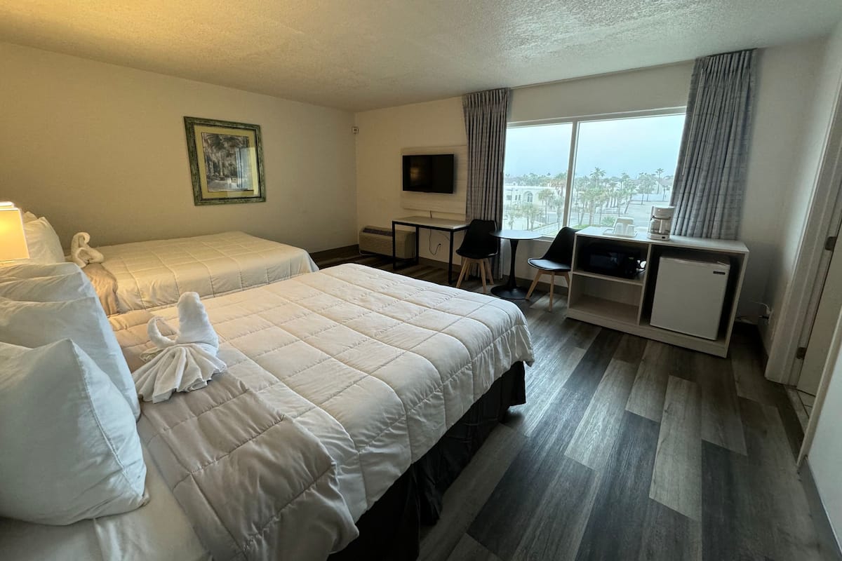 A hotel room with two beds, a desk, a chair, a television, and a view of the city.