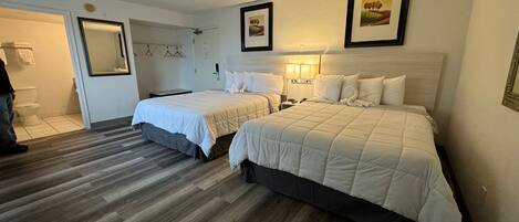 A hotel room with two beds, a bathroom with a toilet and sink, and framed pictures on the wall.
