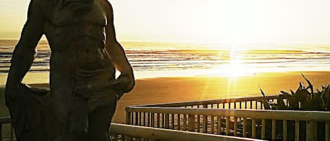 A statue of a man overlooking a beach at sunset.