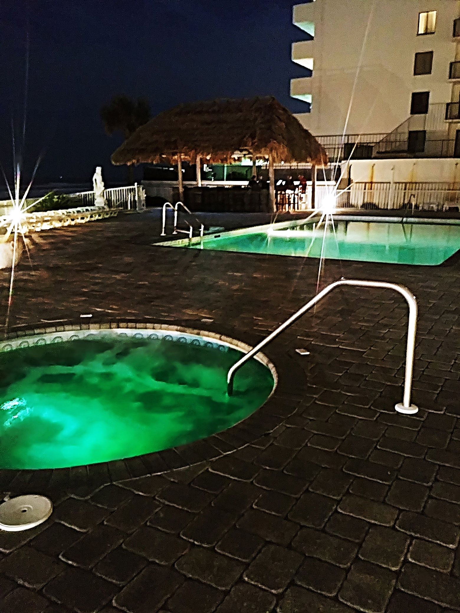 Two outdoor swimming pools with a thatched-roof structure in the background.