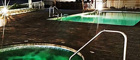 Two outdoor swimming pools with a thatched-roof structure in the background.