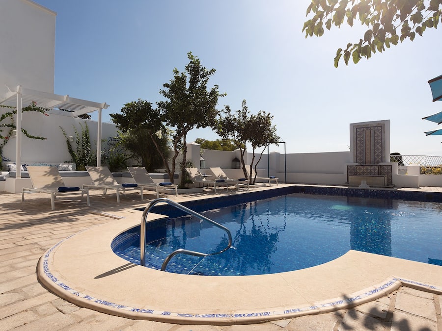 A swimming pool with a tiled edge, lounge chairs, and umbrellas.
