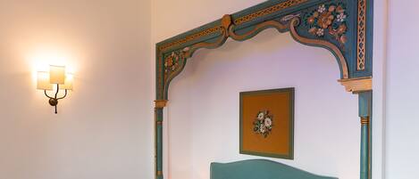Una cama bien tendida con ropa de cama floral, un cabecero decorativo y una lámpara de pared.