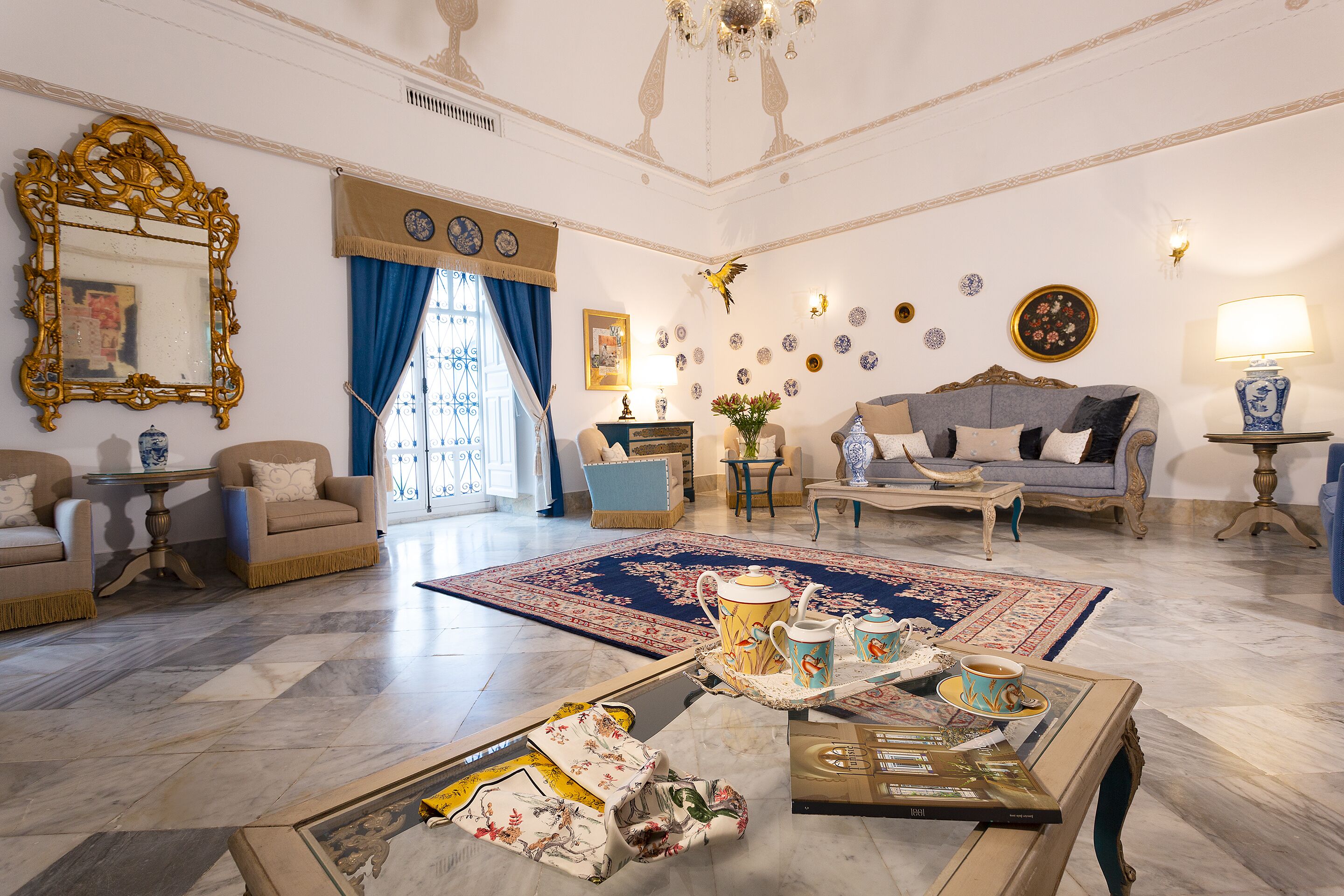 A spacious living room with a large blue rug, a coffee table with a tray of tea cups, and a sofa set.