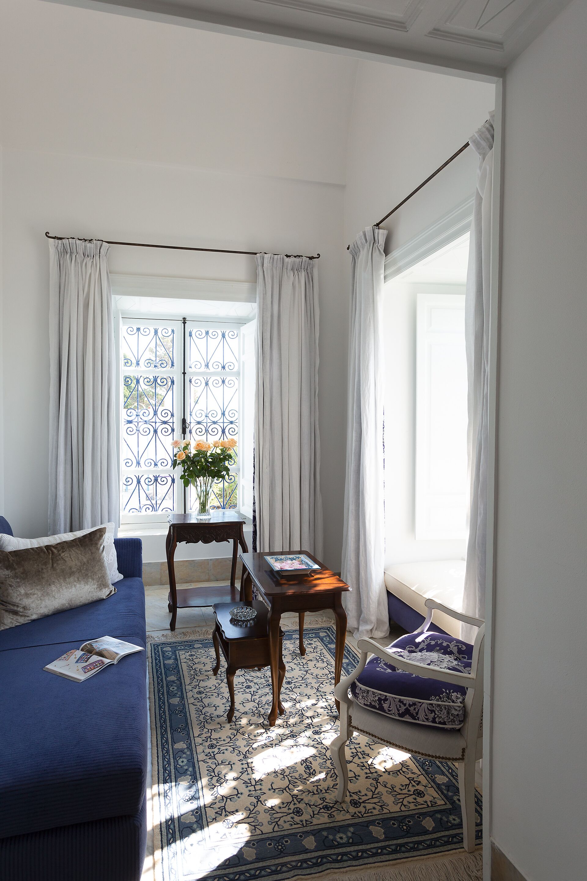 A room with a blue sofa, a small table with a vase of flowers, and a chair with a patterned cushion.