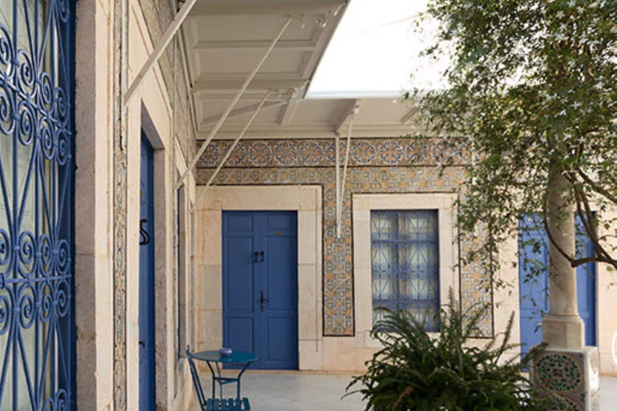 Un patio con una puerta azul, una mesa y una silla azules, y una planta en maceta.
