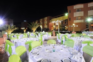 An outdoor banquet hall with round tables set for dining, surrounded by green chairs, and illuminated by overhead lights. - Hotel du Parc (Tunis)