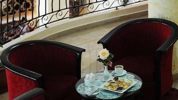 Un coin repas avec deux chaises à revêtement rouge, une petite table ronde agrémentée d’un arrangement floral, et une rambarde à motifs en arrière-plan.