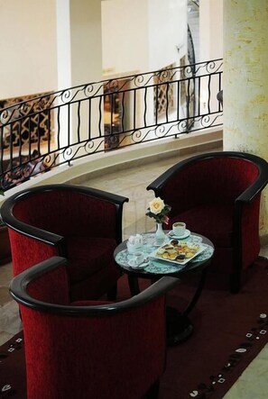 A dining area with two red upholstered chairs, a small round table with a floral centerpiece, and a patterned railing in the background.