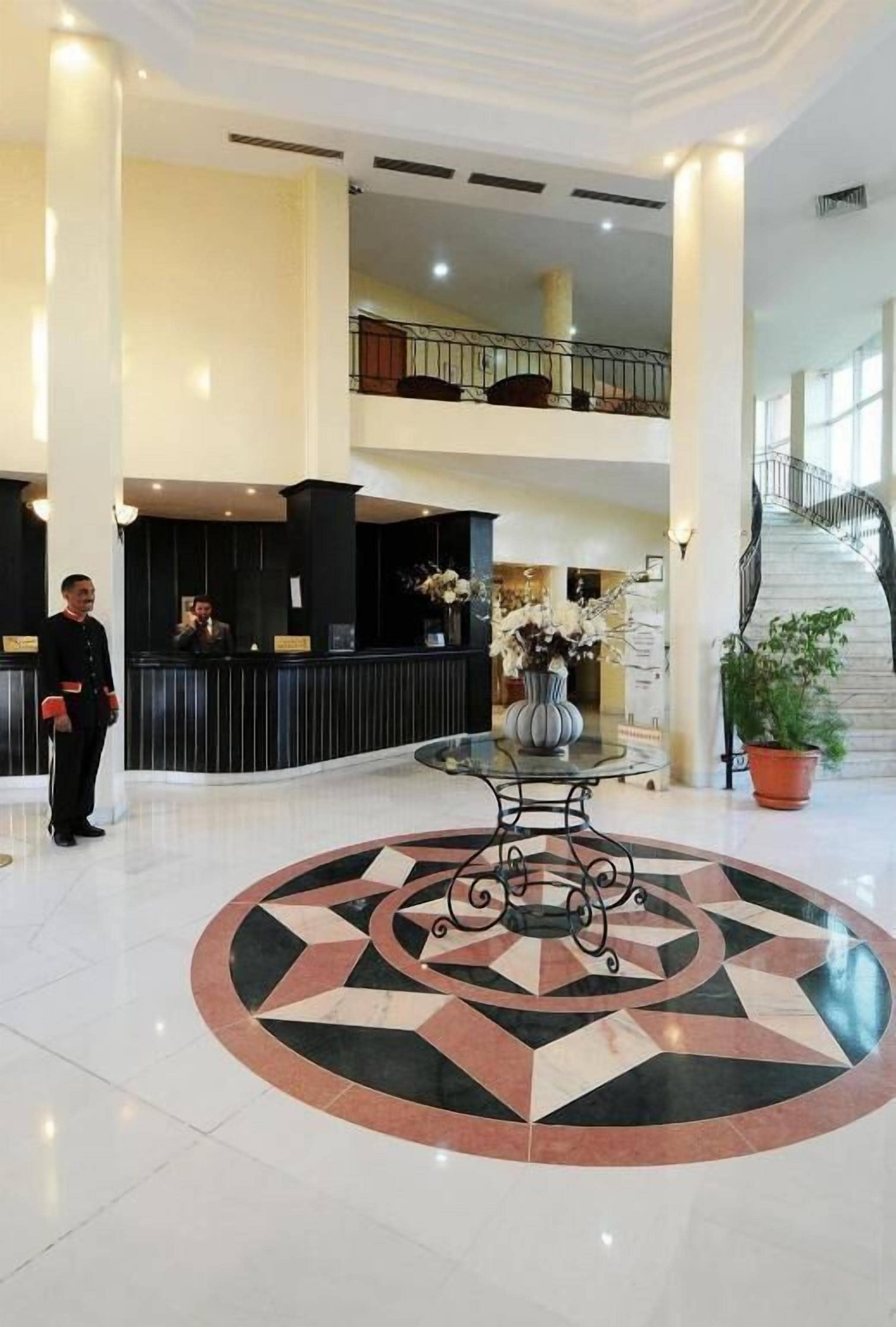 Vestíbulo de hotel con mostrador de recepción, una escalera y un diseño decorativo en el suelo.