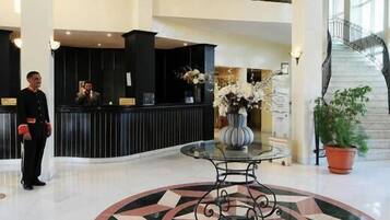 Vestíbulo de hotel con mostrador de recepción, una escalera y un diseño decorativo en el suelo.