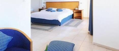 A hotel room with a bed, a seating area with a table, and a view of the adjacent room.