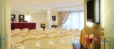 A hotel lobby with rows of white chairs, a reception desk, and a television mounted on the wall.