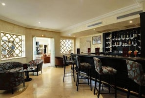 A bar area with a counter, bar stools, and a wine rack with bottles. - Hotel du Parc (Tunis)