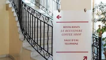 Ein Hotelinnenraum mit einer Treppe, einem Wegweiser, der den Weg zu Restaurants, einem Café und den Zimmern 101 bis 123 zeigt.