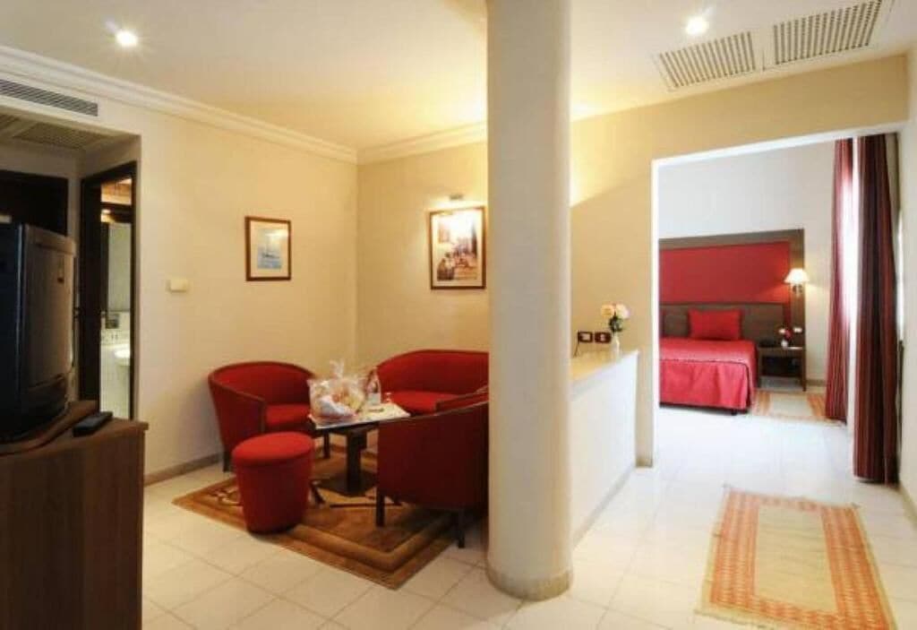 A hotel room with a bed, a TV, a seating area with chairs, and a small table.