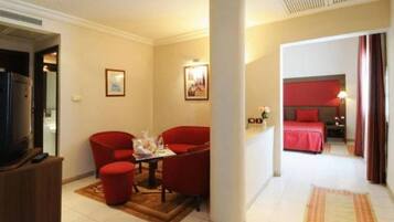 A hotel room with a bed, a TV, a seating area with chairs, and a small table.