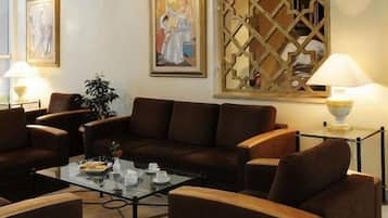 Un espace détente moderne avec un ensemble de canapés marron, une table basse en verre et deux lampes fixées au mur.