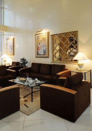 A modern lounge area with a brown sofa set, a glass coffee table, and two wall-mounted lamps. - Hotel du Parc (Tunis)
