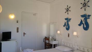 Un dormitorio con cama, escritorio, silla, televisor, armario y espejo, además de adornos en la pared como un timón de barco y figuras de sirenas.