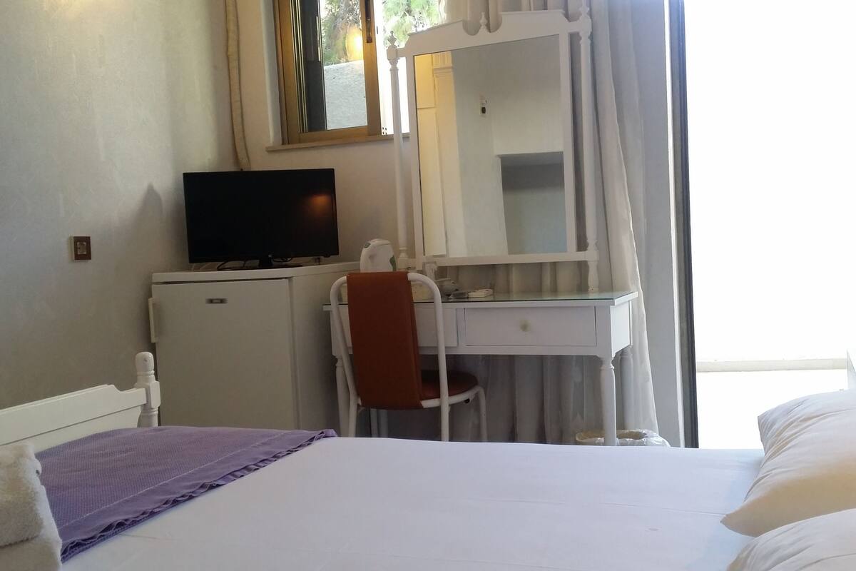 A hotel room with a bed, a desk with a chair, a television, and a window with curtains.