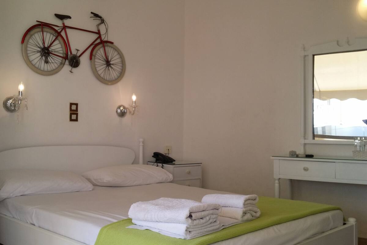 A hotel room with a bed, a nightstand, a mirror, and a bicycle mounted on the wall.