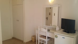 A small, white bedroom with a single bed, a bedside table with a mirror, a TV, and a small trash bin. - Hotel Rachel (Aegina)
