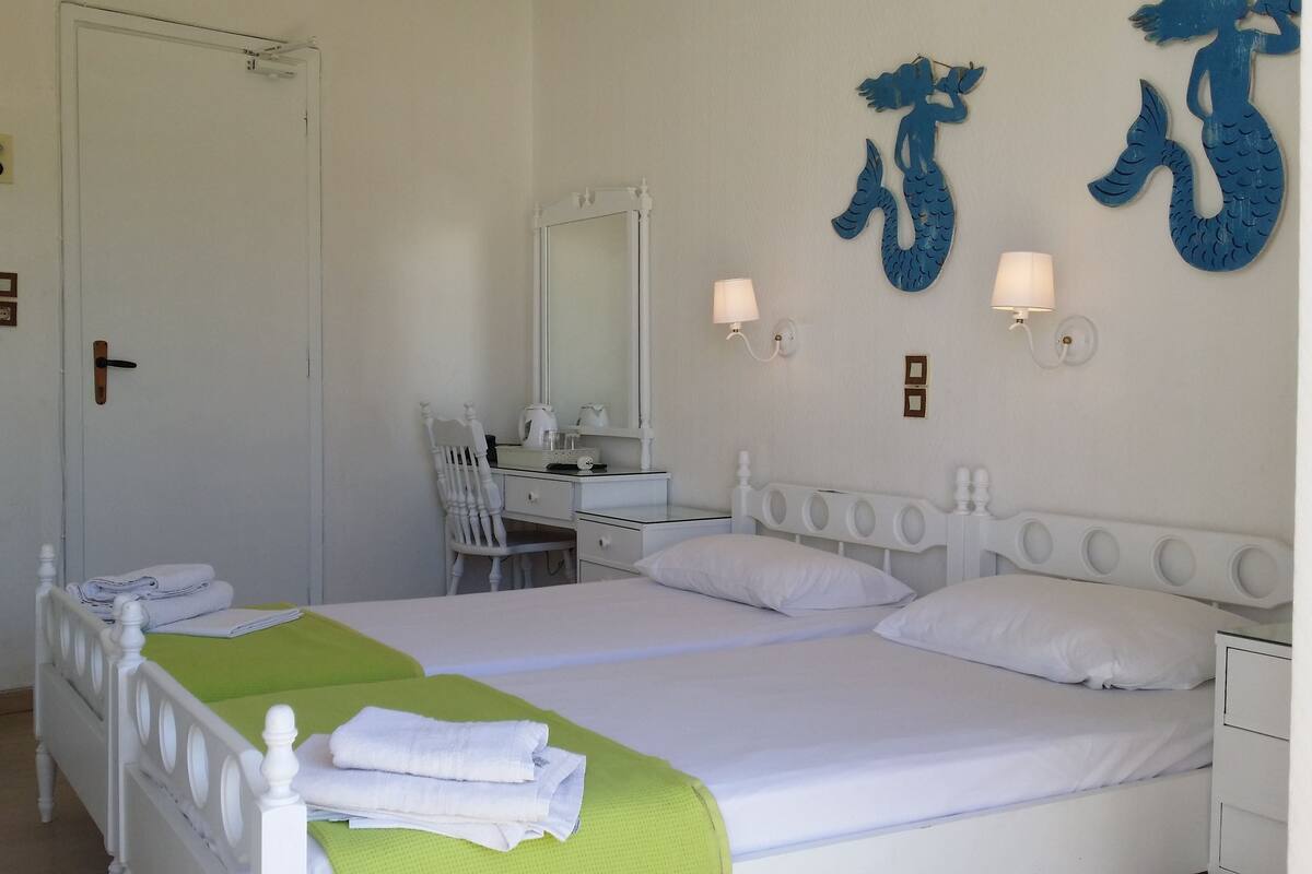 A hotel room with a bed, two bedside tables, a desk with a chair, a television, and a large mirror.