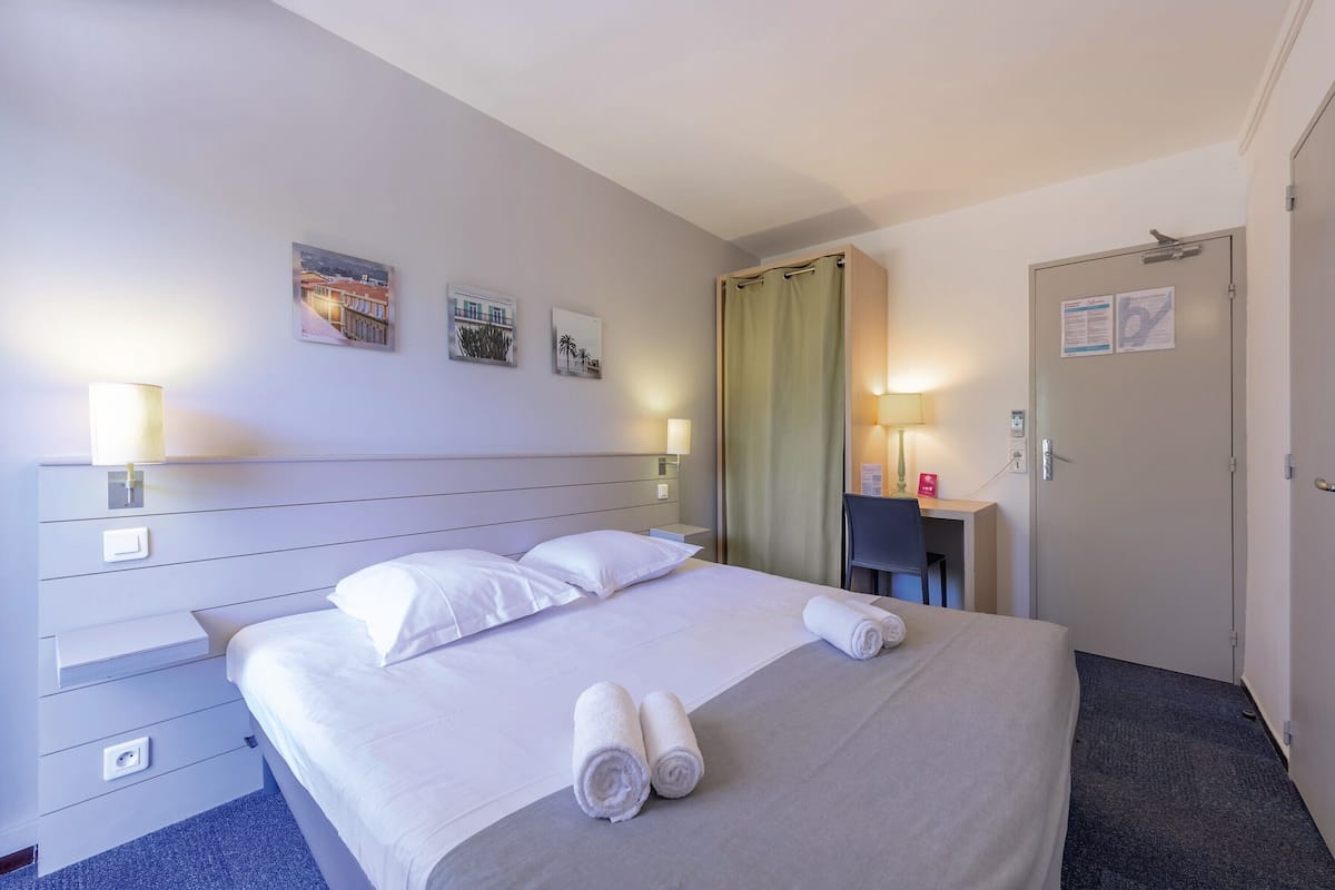 Una habitación de hotel con una cama, dos lámparas de noche, un escritorio, una silla y una puerta con cerradura y lector de tarjeta.