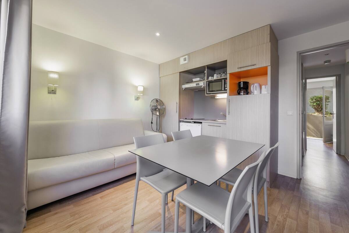 Una sala moderna con un sofá, una mesa de comedor con sillas y una cocina equipada.