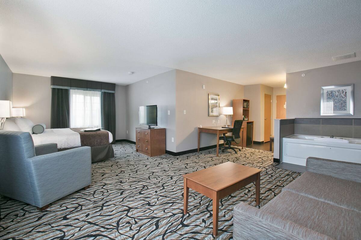 A hotel room with a bed, a sofa, a desk, a TV, a dresser, and a bathroom with a bathtub.