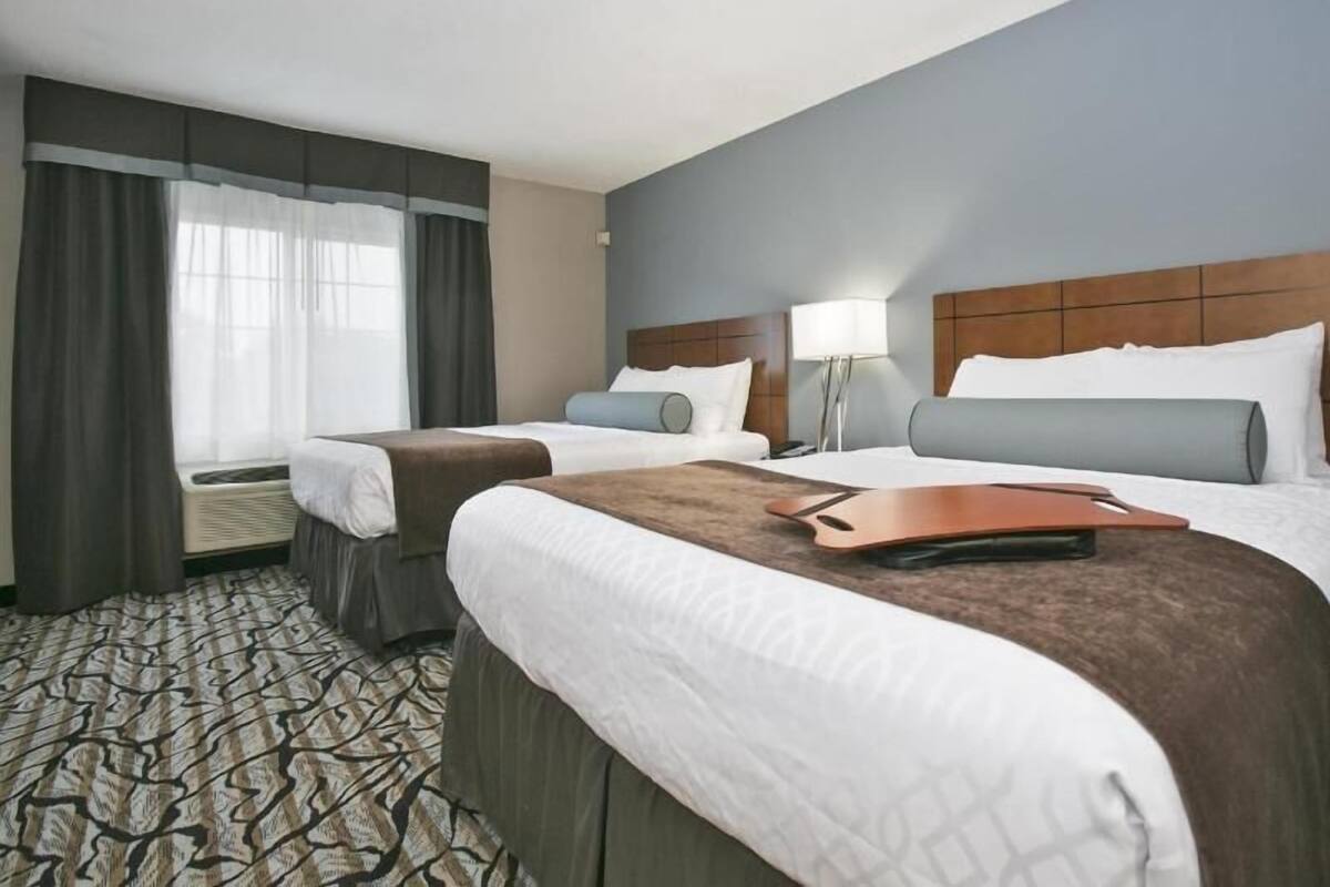A hotel room with two beds, a window with curtains, a lamp, and a patterned carpet.