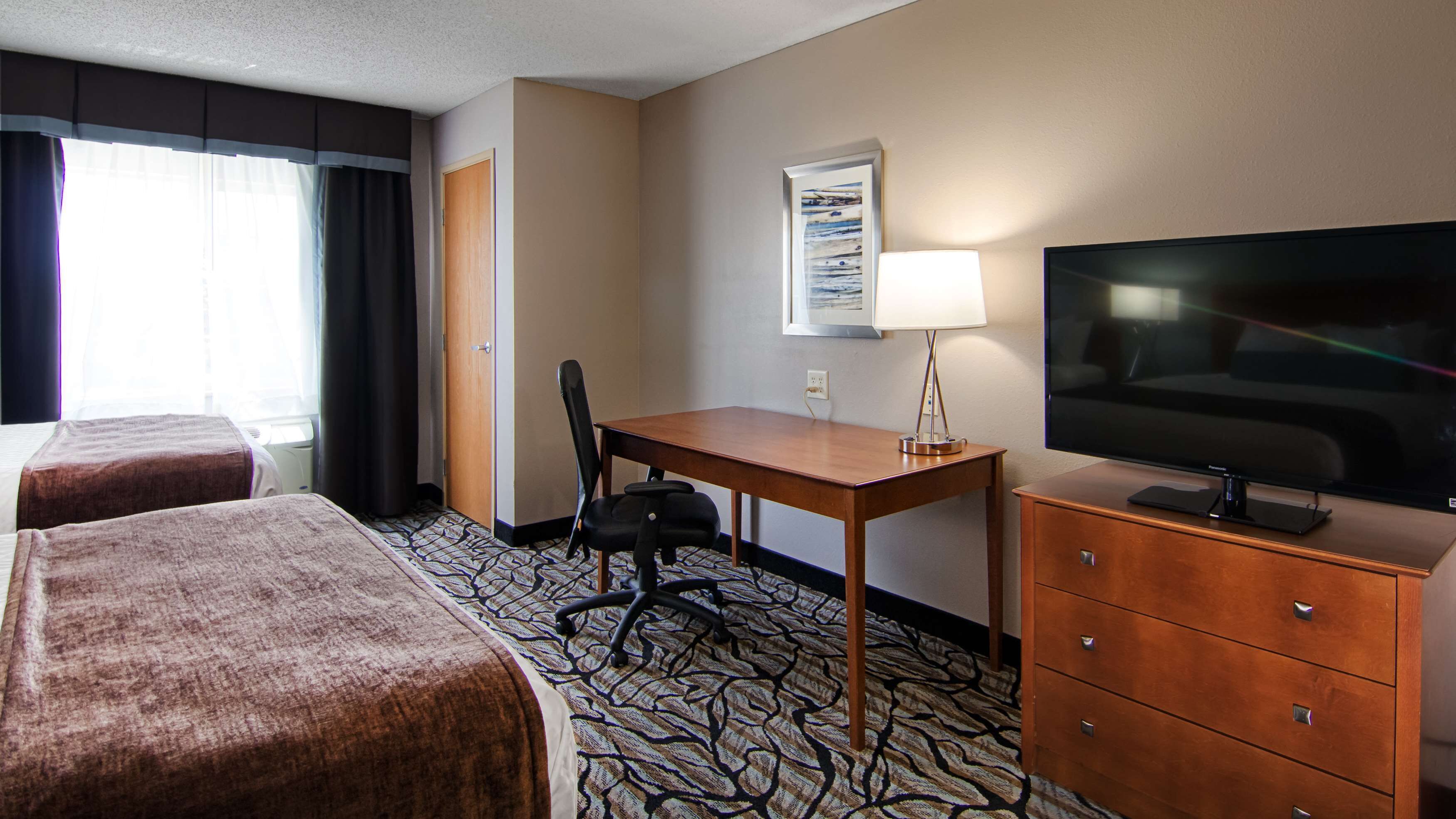 A hotel room with two beds, a desk, a chair, a TV, and a dresser.
