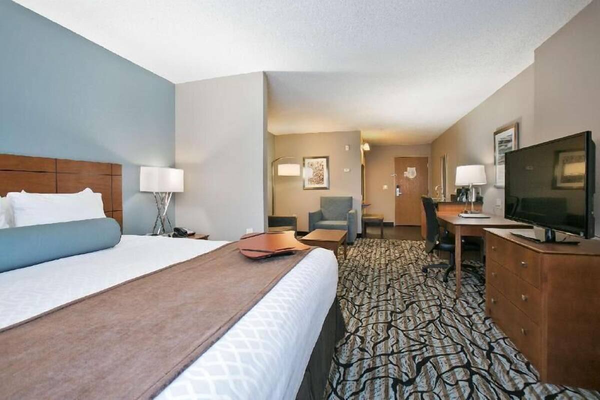 A hotel room with a large bed, a desk with a computer, a television, and a chair.