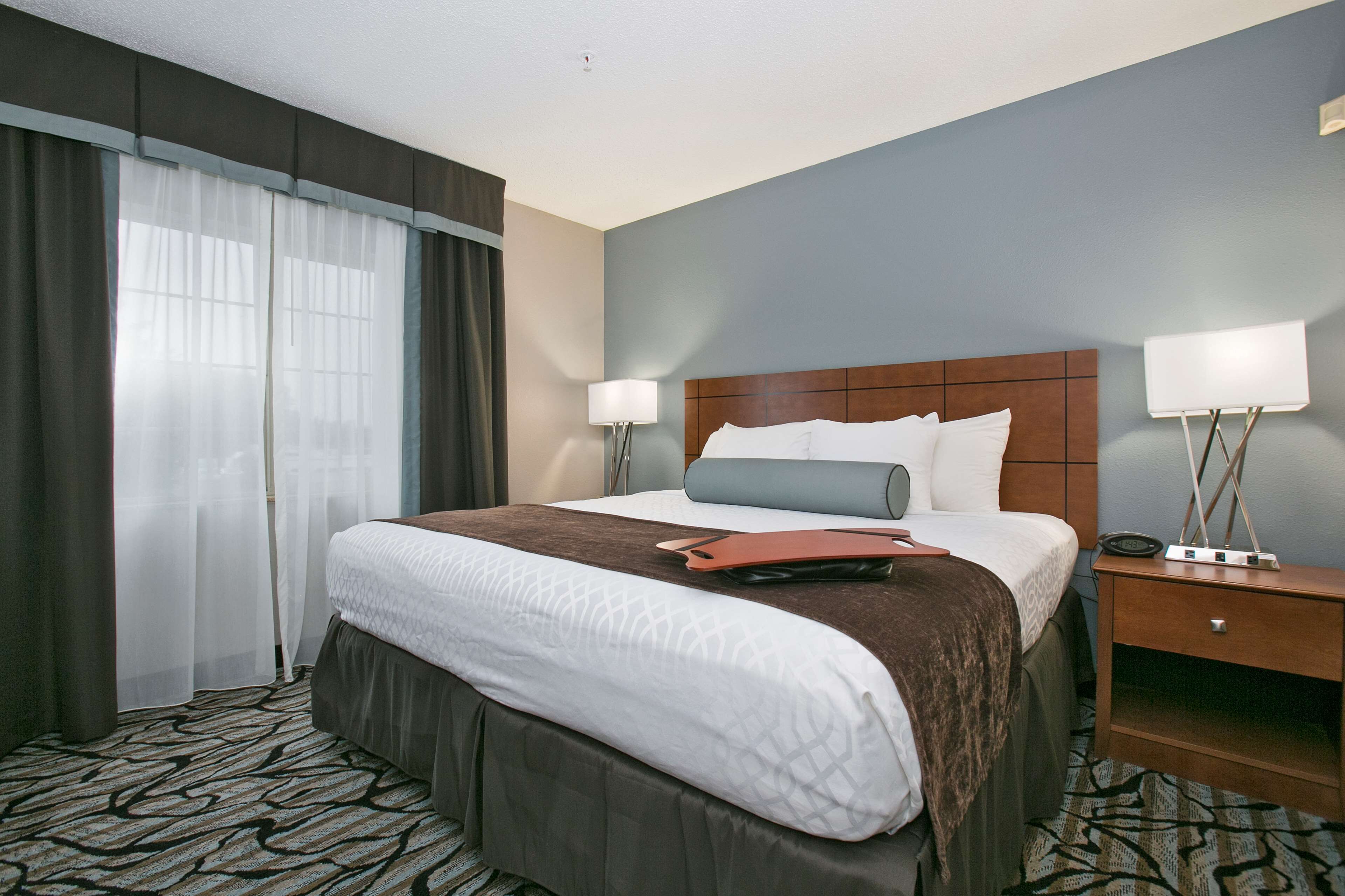 Habitación de hotel con una cama grande, dos mesitas de noche con lámparas, una alfombra estampada y una ventana con cortinas.