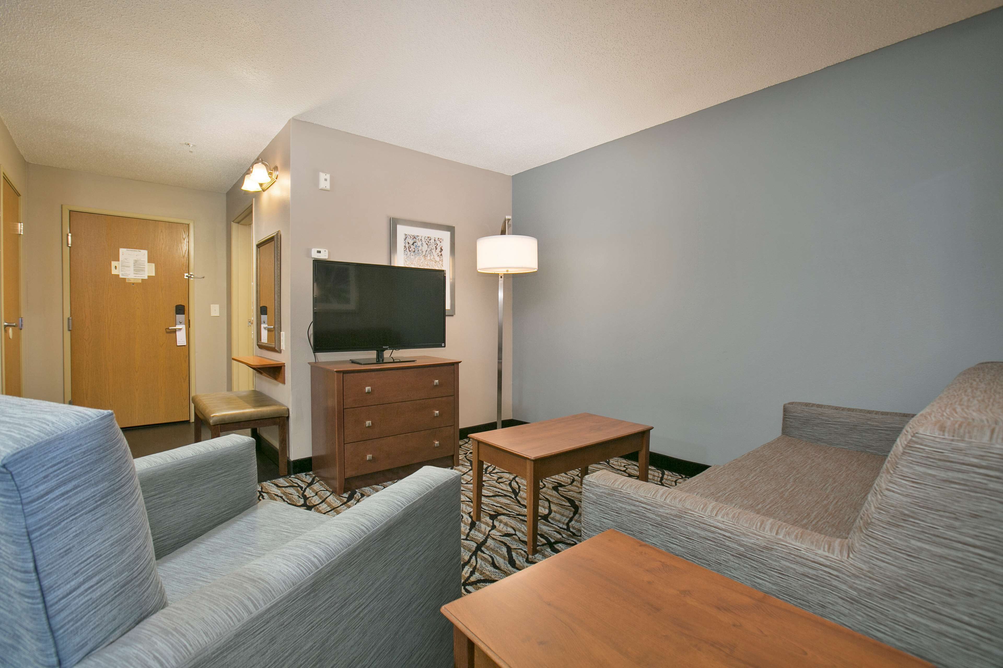 Een hotelkamer met twee banken, een houten tafel, een televisie, een dressoir en een lamp.