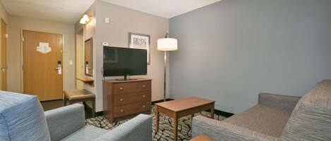 A hotel room with two sofas, a wooden table, a TV, a dresser, and a lamp.