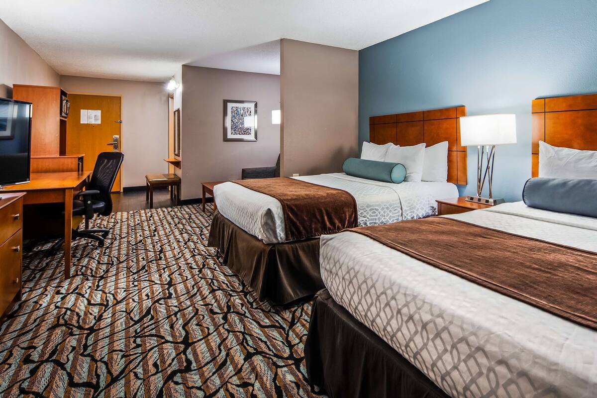 A hotel room with two beds, a desk, a chair, a television, and a patterned carpet.