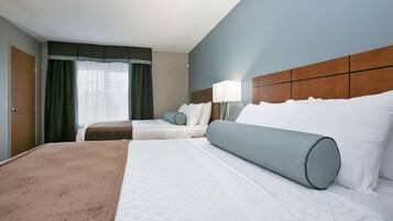 A hotel room with two beds, a large window with curtains, a wooden headboard, and a bedside lamp.