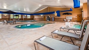 Piscina interior con sillones de descanso y sombrillas, rodeada de pavimento y paredes de piedra.
