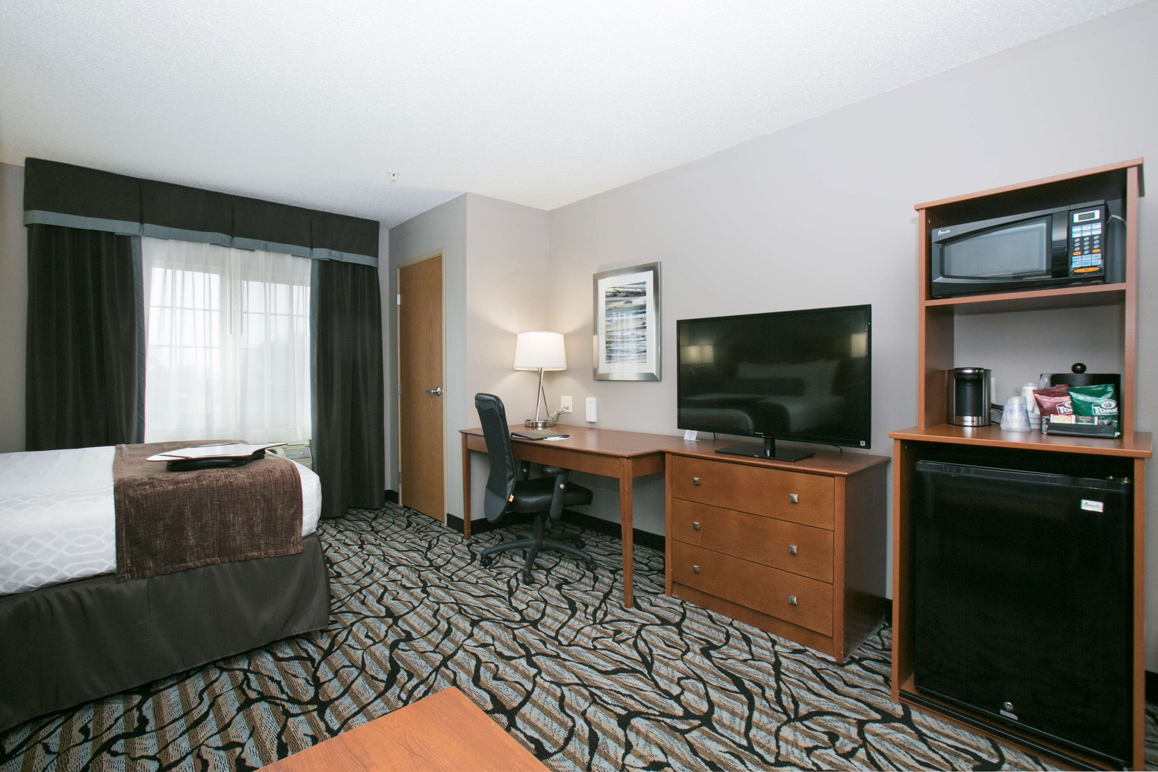 A hotel room with a bed, desk, chair, television, microwave, and refrigerator.