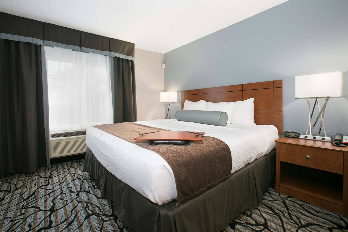 A hotel room with a large bed, a bedside table with a lamp, and a window with curtains.