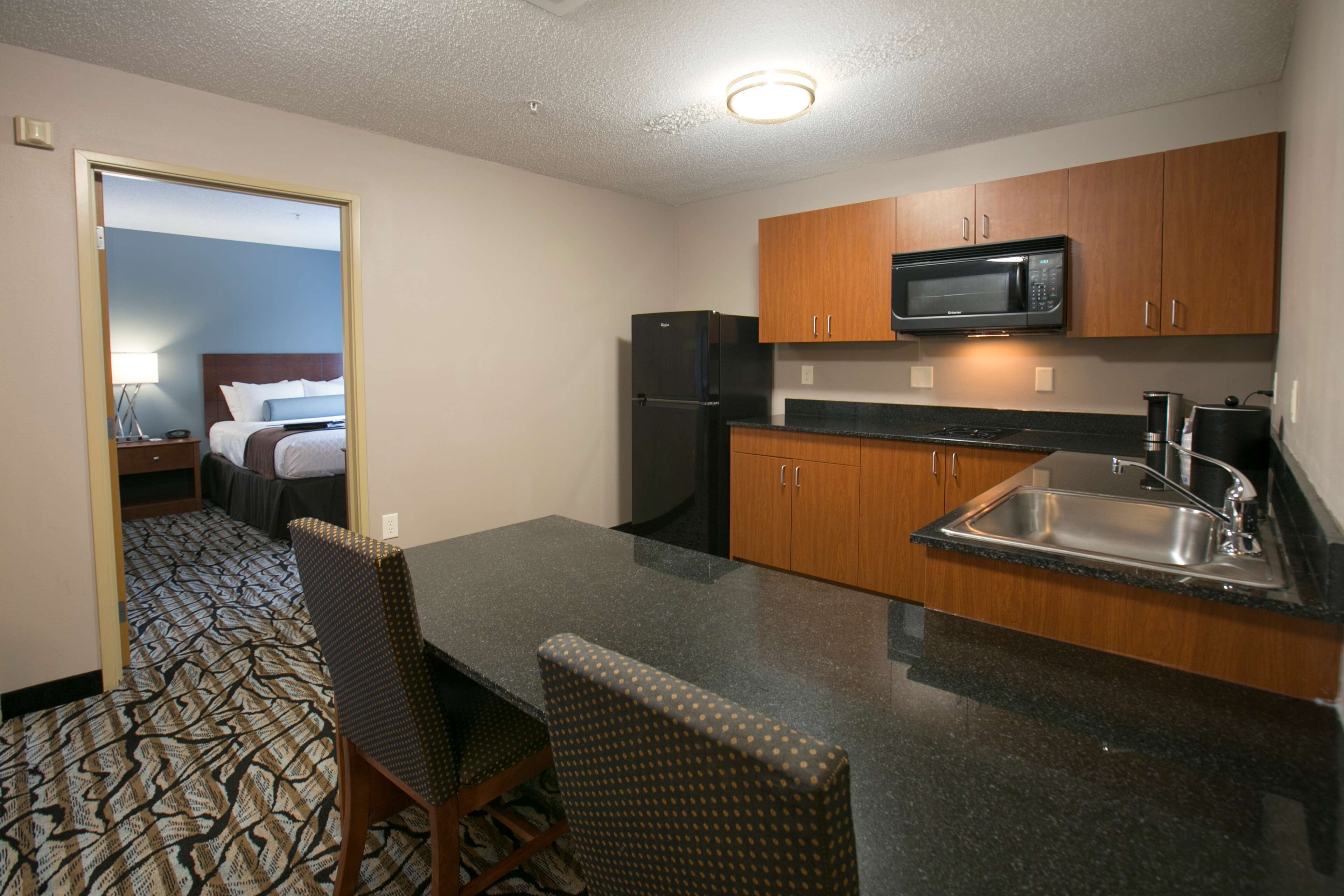 A compact hotel room with a kitchenette, a dining area with a table and chairs, and a bed with a headboard.