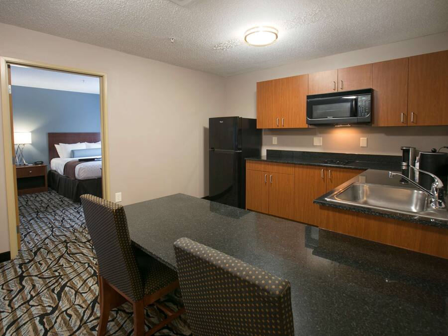 A compact hotel room with a kitchenette, a dining area with a table and chairs, and a bed with a headboard.