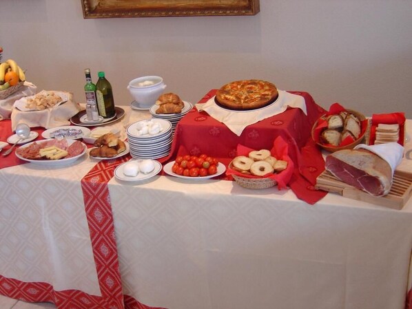 Una mesa dispuesta con diversos alimentos, como pizza, pasteles y carnes, lo que sugiere un servicio de buffet o una comida compartida.