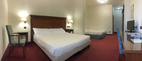 A hotel room with a large bed, two bedside tables, a chair, a desk with a computer, and a small sofa.