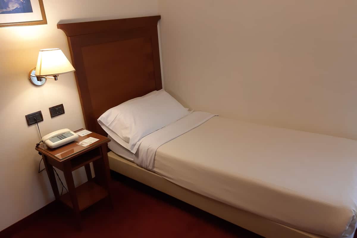 A single bed with a wooden headboard, a bedside table with a lamp, and a phone.
