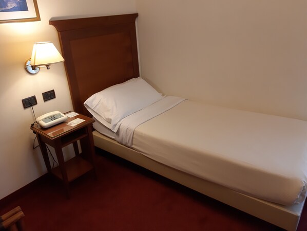 A single bed with a wooden headboard, a bedside table with a lamp, and a phone.