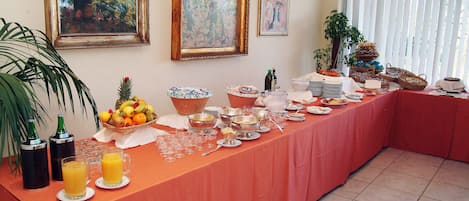 Een buffet met diverse gerechten en drankjes, een kunstwerk op de muur en een potplant.
