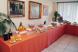Una mesa de buffet con diferentes alimentos y bebidas, una obra de arte enmarcada en la pared y una planta en maceta.